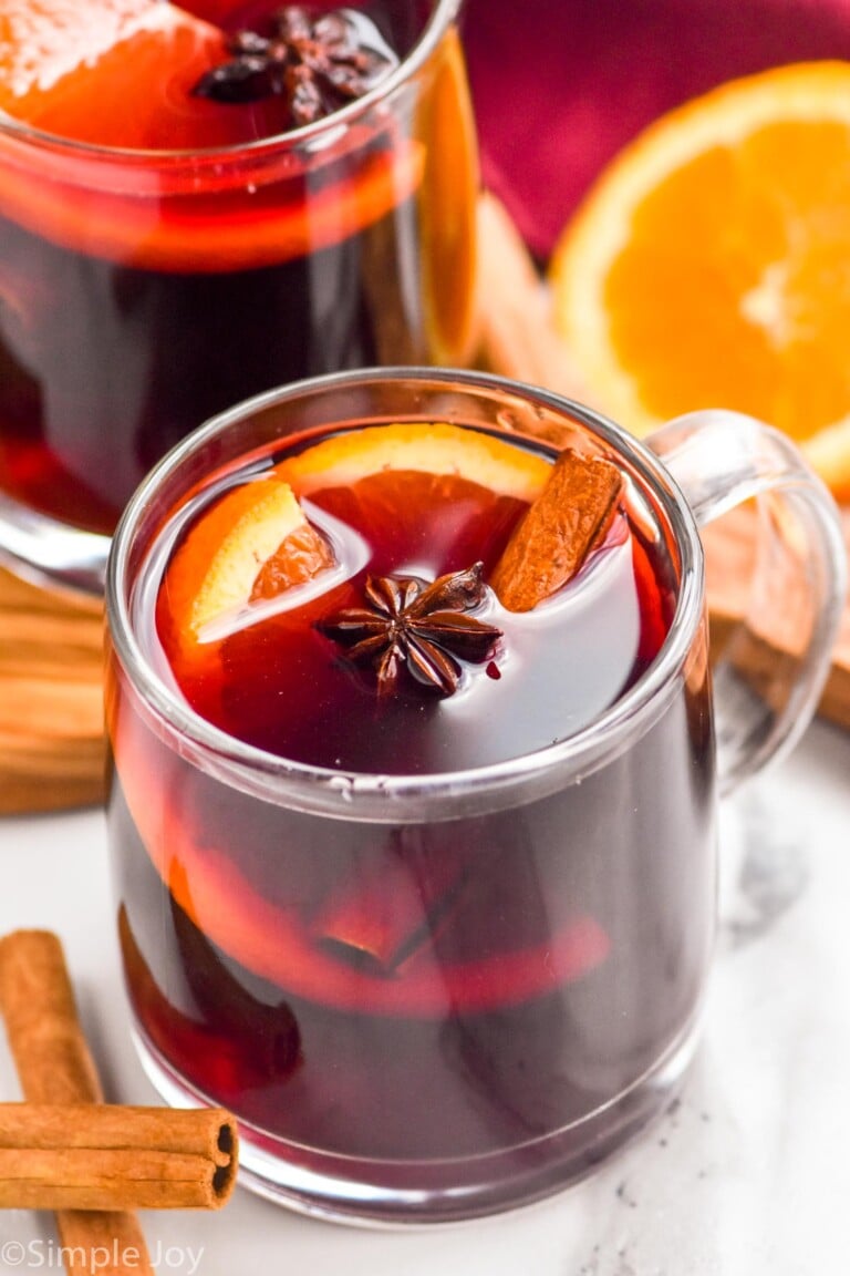 Photo of mugs of Slow Cooker Mulled Wine with cinnamon sticks and oranges beside