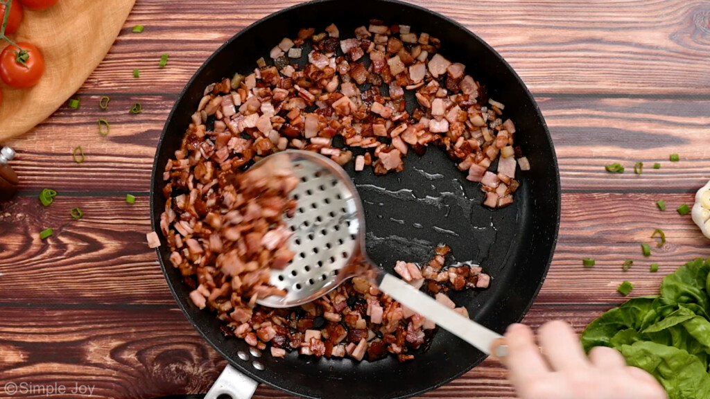 overhead of bacon being removed from a skillet with a slotted spoon