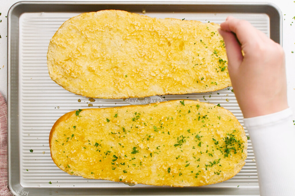 fresh parsley being spread over uncooked garlic bread