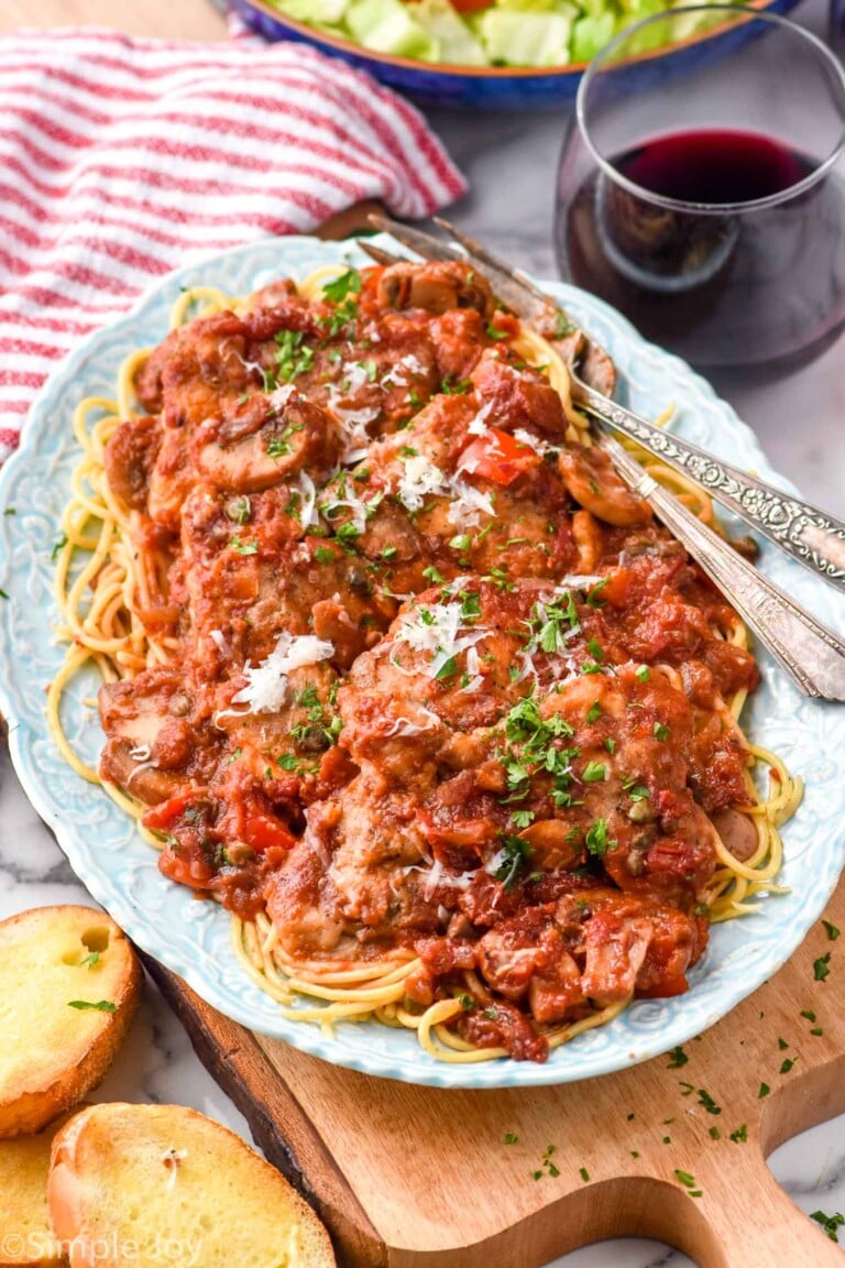 plate of Chicken Cacciatore with a fork for serving. Glasses of red wine and bowl of salad sitting beside.