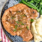 smothered pork chop on a plate with green beans and mashed potatoes