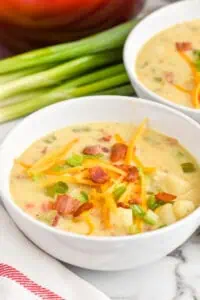 bowl of creamy potato soup with bacon topped with cheese, bacon, and scallions