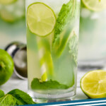 pinterest graphic of up close view of a high ball glass filled with a mojito cocktail, lime slices, fresh mint, striped green straws, and garnished with lime wedges and fresh mint, says: mojito cocktail simplejoy.com