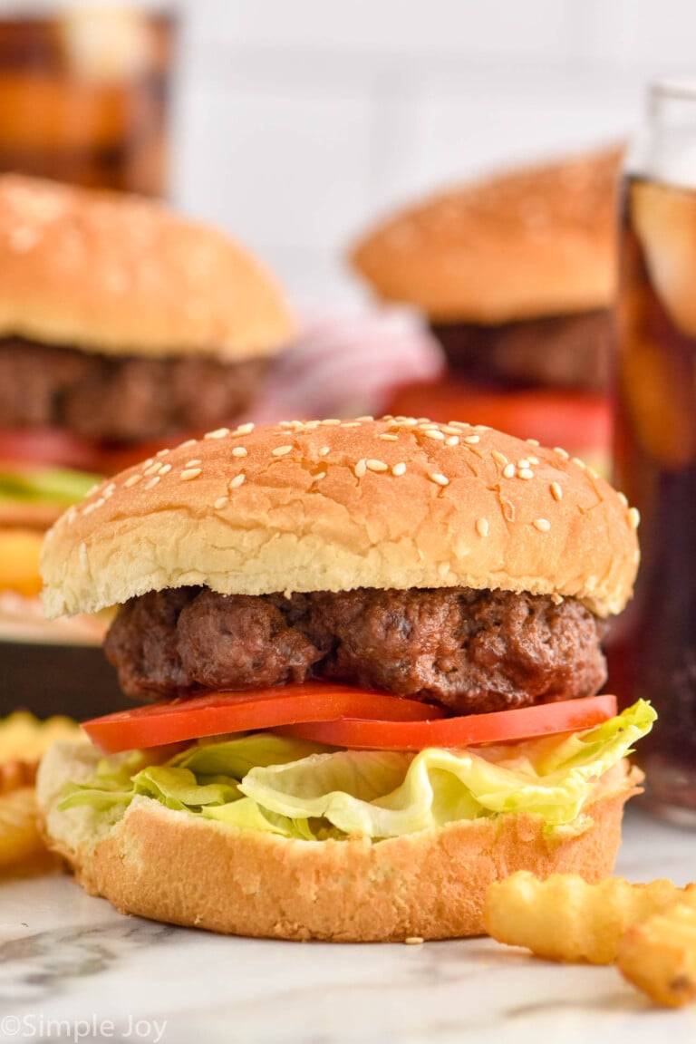 Side view of Air Fryer Burgers served on a bun with lettuce and tomatoes. Fries beside.