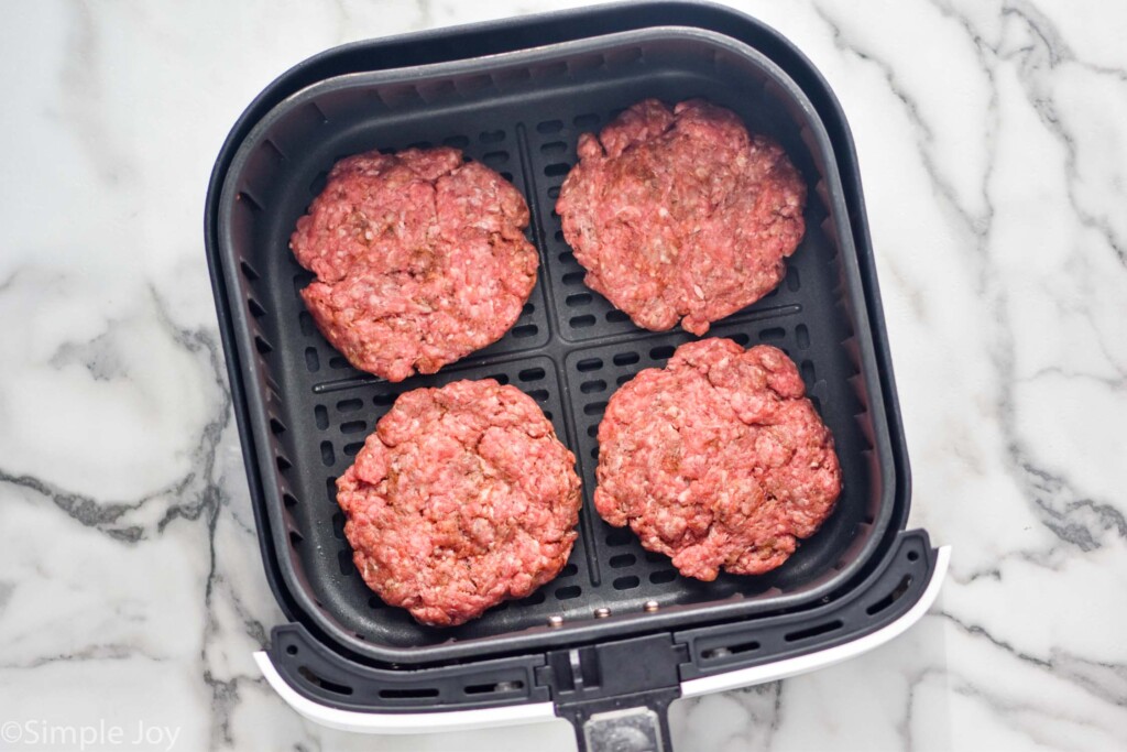 Overhead view of air fryer basket with raw hamburgers for Air Fryer Burgers recipe