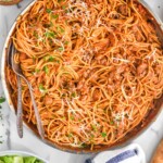 Overhead view of a pot of Sausage Spaghetti in large skillet garnished with parsley and shredded parmesan cheese with salad and parmesan beside. Two forks in skillet for serving.