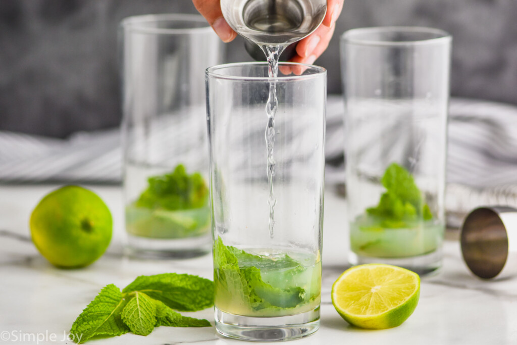 adding rum to a high ball glass with mint and lime juice