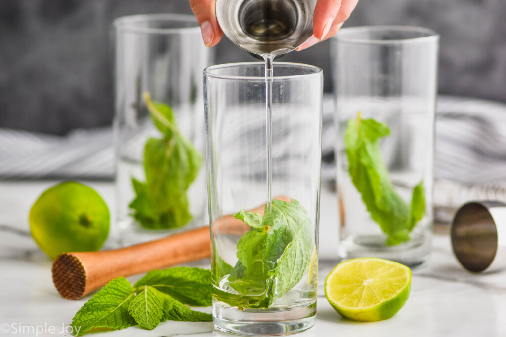 pouring simple syrup into a high ball glass that has mint leaves in it