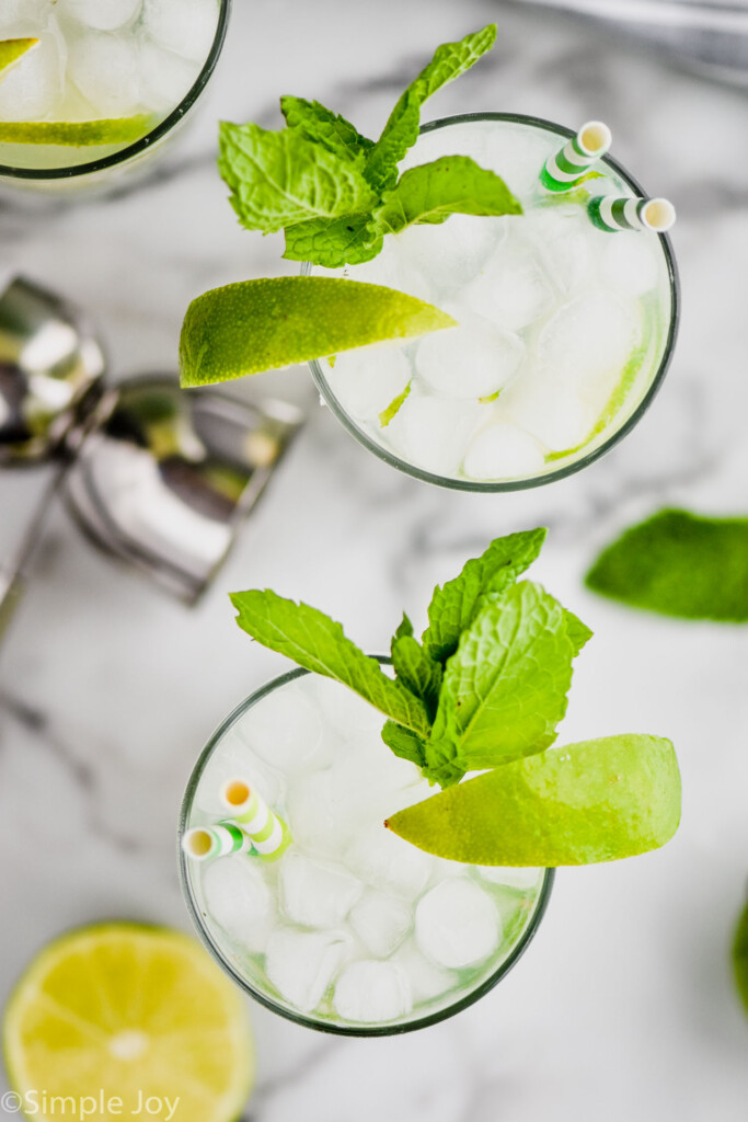 overhead view of two highball glasses filled with the best mojito recipe, ice, lime wedges, and fresh mint