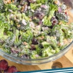 Pinterest graphic for Broccoli Salad recipe. Image shows a glass bowl of Broccoli Salad with grapes and wooden spoon beside. Text says, "Broccoli Salad simplejoy.com"
