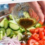 Pinterest graphic for Cucumber Tomato Salad. Text says "the best Cucumber Tomato Salad simplejoy.com" Image shows man's hand pouring small bowl of dressing into a bowl of Cucumber Tomato Salad ingredients.