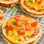 Mexican pizzas topped with diced tomato, green onions, and fresh cilantro sitting on wire cooling rack.