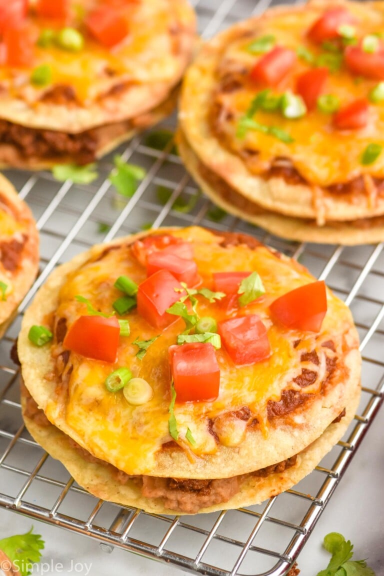 Mexican pizzas topped with diced tomato, green onions, and fresh cilantro sitting on wire cooling rack.