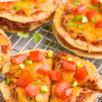 Pinterest graphic for mexican pizza. Image shows Mexican pizzas topped with diced tomato, green onions, and fresh cilantro sitting on wire cooling rack. Text says "copycat mexican pizza simplejoy.com"