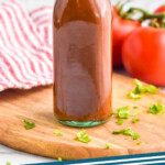 pinterest graphic for taco sauce. Image shows a bottle of taco sauce with tomatoes sitting in background. Text says "homemade taco sauce simplejoy.com"