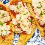 three pieces of Air Fryer Chicken Parmesan on a plate topped with marinara sauce, cheese, and fresh parsley