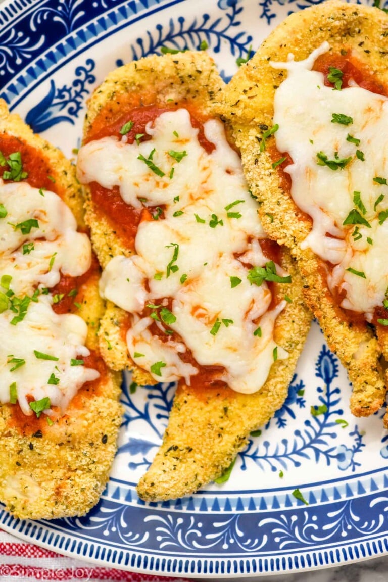 three pieces of Air Fryer Chicken Parmesan on a plate topped with marinara sauce, cheese, and fresh parsley