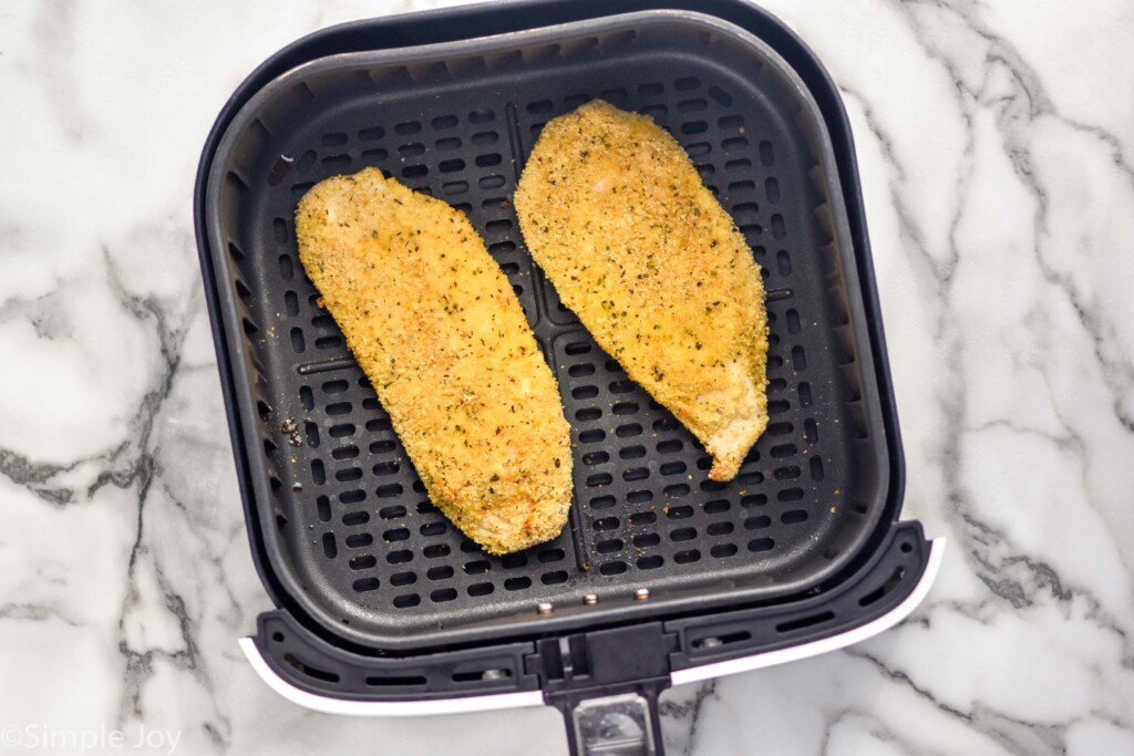 overhead of air fryer basket with two pieces of chicken to make Air Fryer Chicken Parmesan