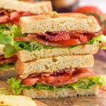 Side view of BLT sandwich cut in half and stacked on top of each other on a wooden board. Chips beside.