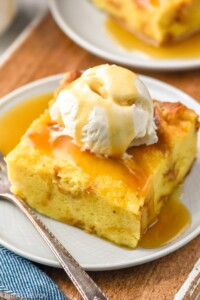 Bread Pudding on a plate served with ice cream and Bread Pudding sauce with a fork beside.