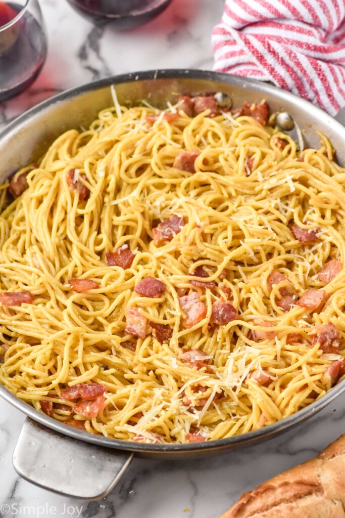 Large pan of Pasta Carbonara with bread and glasses of wine beside.