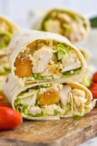 Side view of Chicken Caesar Wrap sliced in half and stacked on top of each other. Tomatoes beside