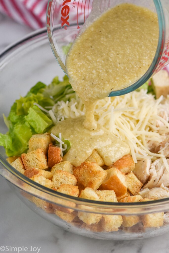 Ingredients for Chicken Caesar Wrap filling in a glass bowl with glass measuring cup of dressing being poured on top