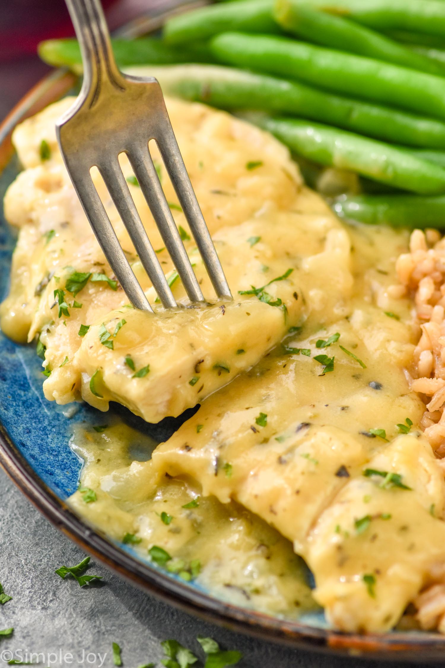 fork holding piece of honey mustard chicken on a plate with green beans and rice.