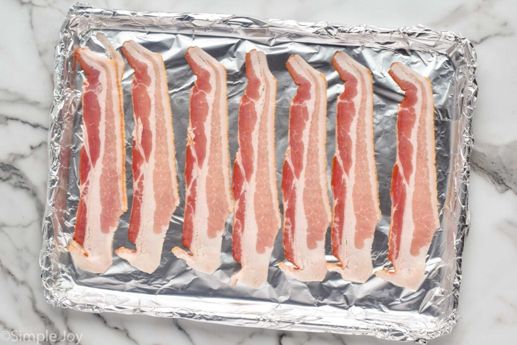 overhead of baking sheet covered with foil and strips of bacon to make Bacon in The Oven