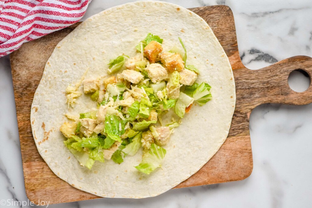 Overhead view of Chicken Caesar Wrap being made on a wooden board.