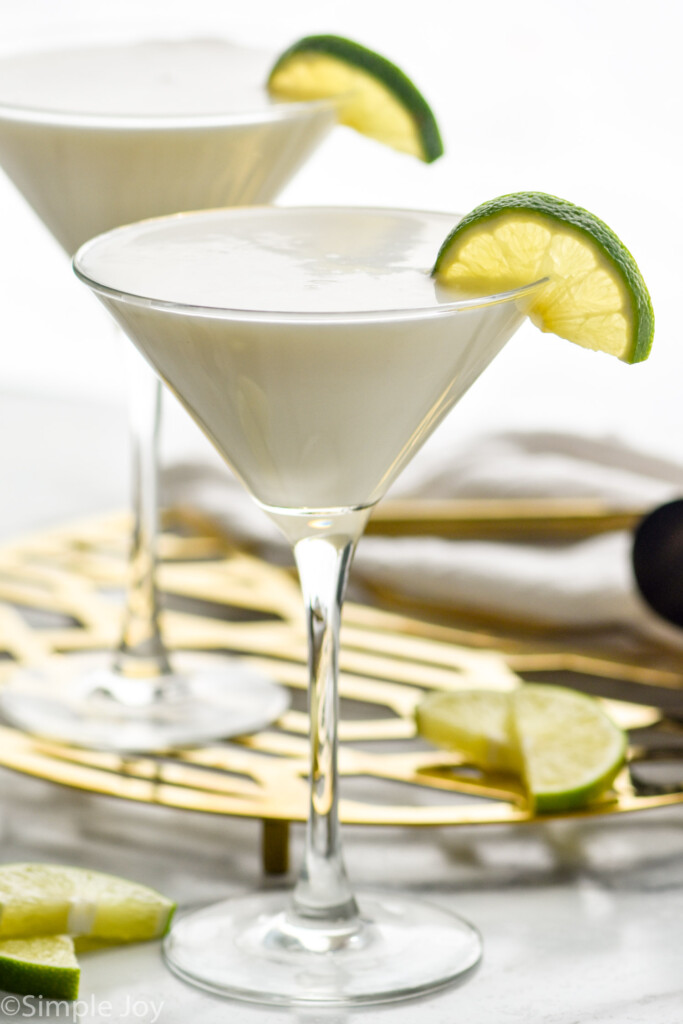 Key Lime Martinis garnished with slices of lime. Additional slices of lime and cocktail jigger beside.