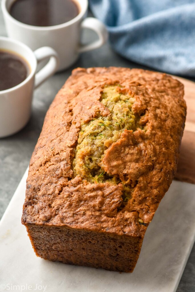 loaf of Zucchini Bread on a cutting board with mugs of coffee sitting in background