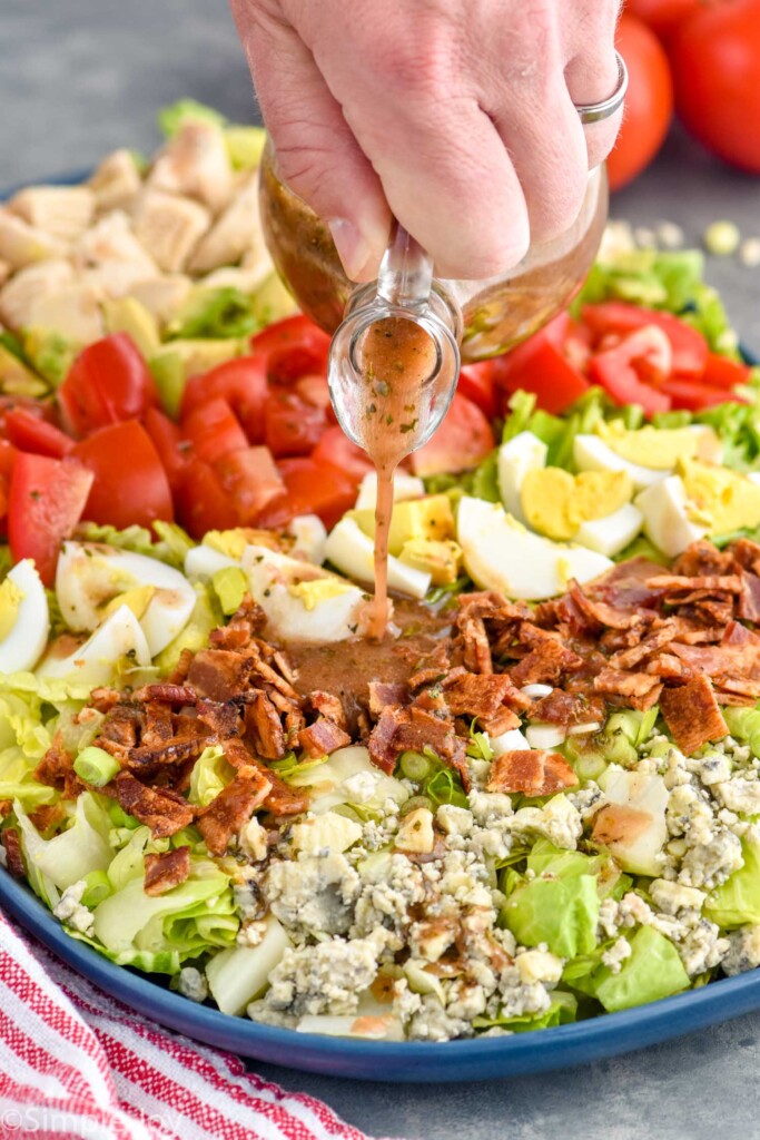 Person's hand pouring Red Wine Vinaigrette over cobb salad