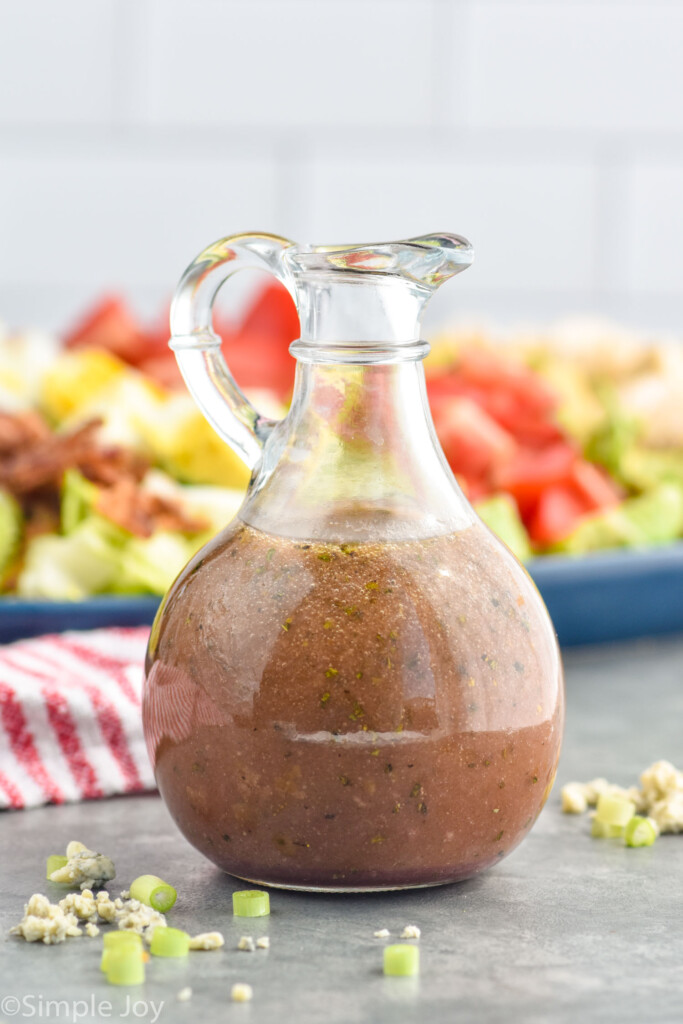 Side view of a jar of Red Wine Vinaigrette with cobb salad behind