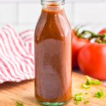 bottle of homemade Taco Sauce on a wooden board, tomatoes sitting in background