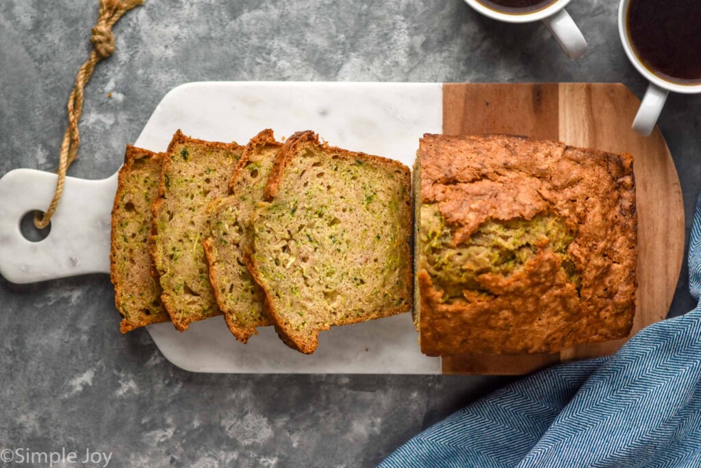 overhead of loaf and slices of zucchini bread on a cutting board with mugs of coffee sitting beside