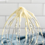 pinterest graphic of a whisk with cream cheese frosting on it, says: "the best cream cheese frosting simplejoy.com"