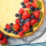 Pinterest graphic for Easy Cheesecake Recipe. Image shows overhead of Easy Cheesecake Recipe topped with fresh strawberries, raspberries, and blueberries. Text says "Vanilla cheesecake simplejoy.com"