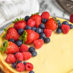 Pinterest graphic for Easy Cheesecake Recipe. Text says "the best cheesecake recipe simplejoy.com" Image shows a homemade cheesecake topped with fresh blueberries, strawberries, and raspberries.