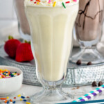 Pinterest graphic for homemade Milkshakes. Image shows a vanilla milkshake with a strawberry milkshake, chocolate milkshake, bowl of sprinkles, and fresh strawberries sitting in background. Text says "the best milkshakes simplejoy.com"