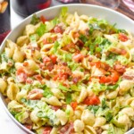 bowl of BLT Pasta Salad with two drinks sitting behind and fresh tomatoes in front