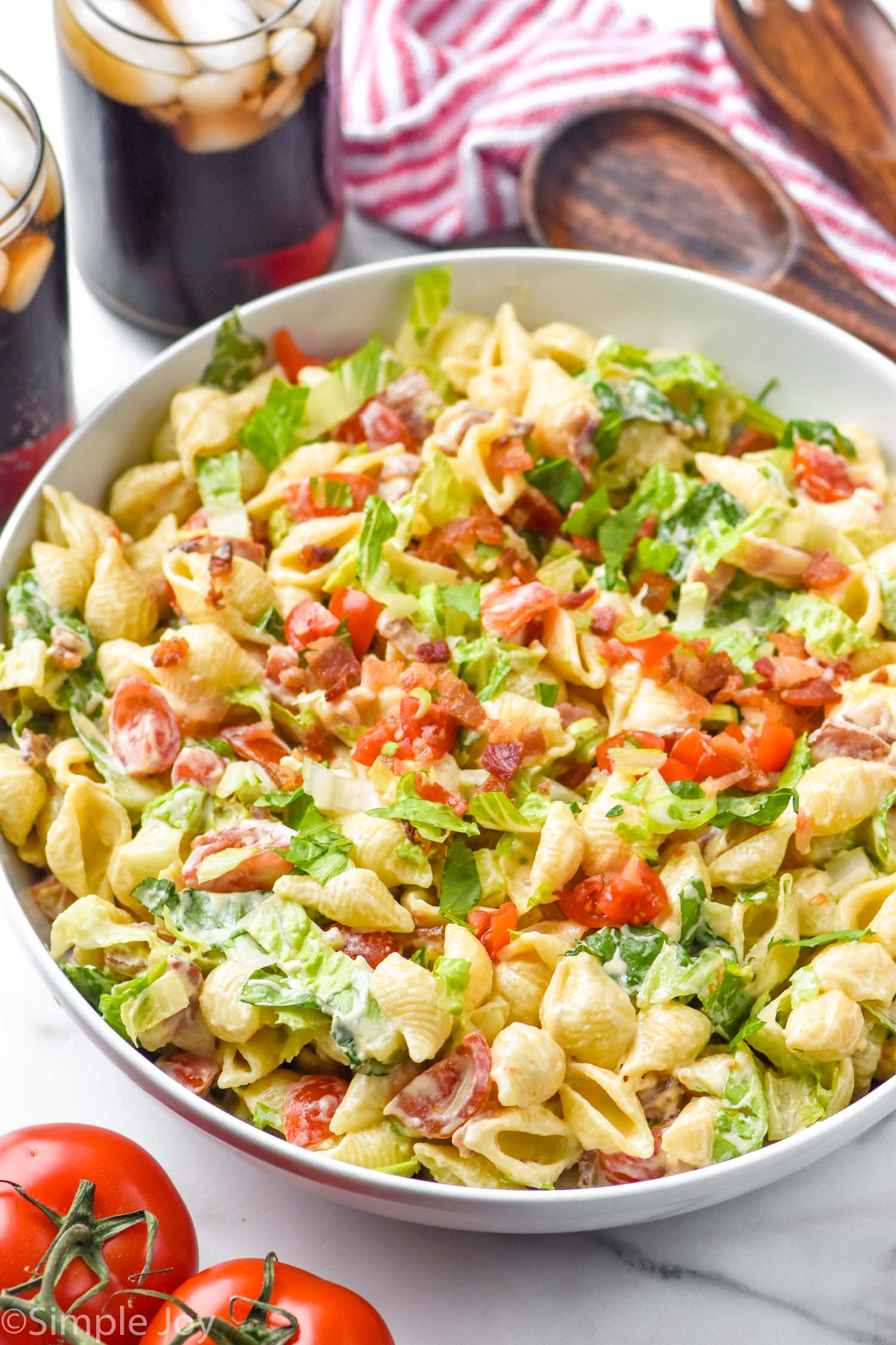 bowl of BLT Pasta Salad with two drinks sitting behind and fresh tomatoes in front