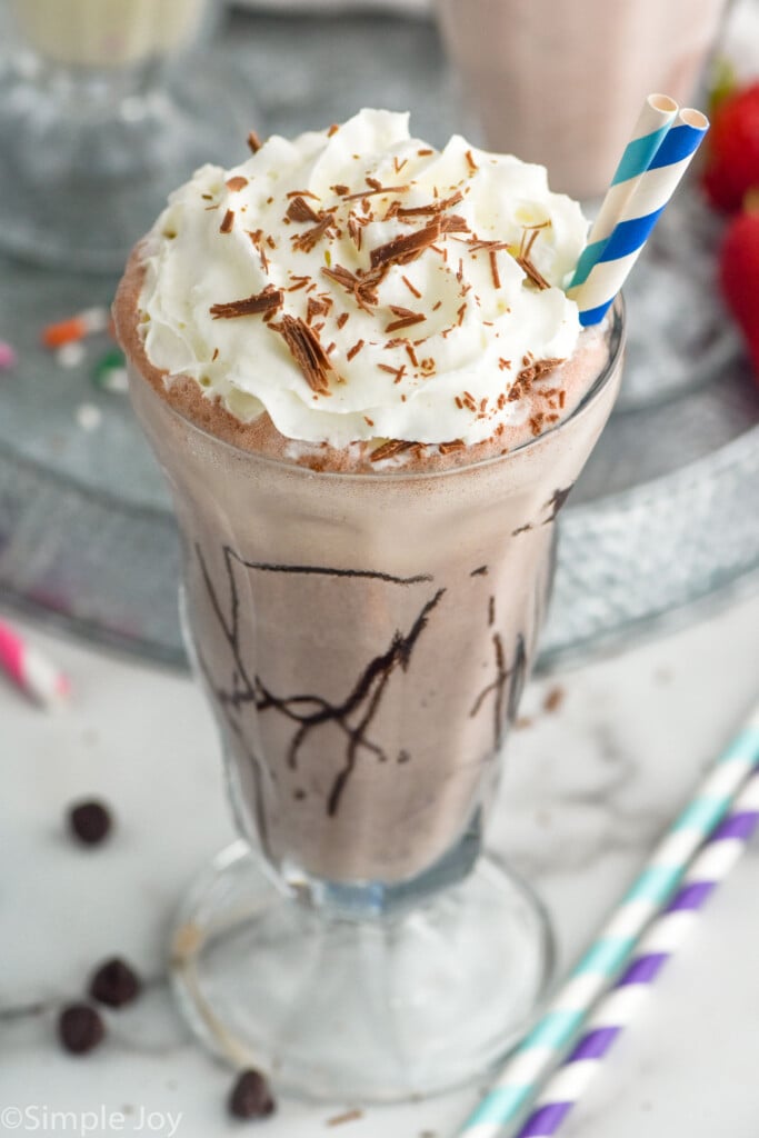 Glass of chocolate Milkshake topped with whipped cream and chocolate shavings with two straws