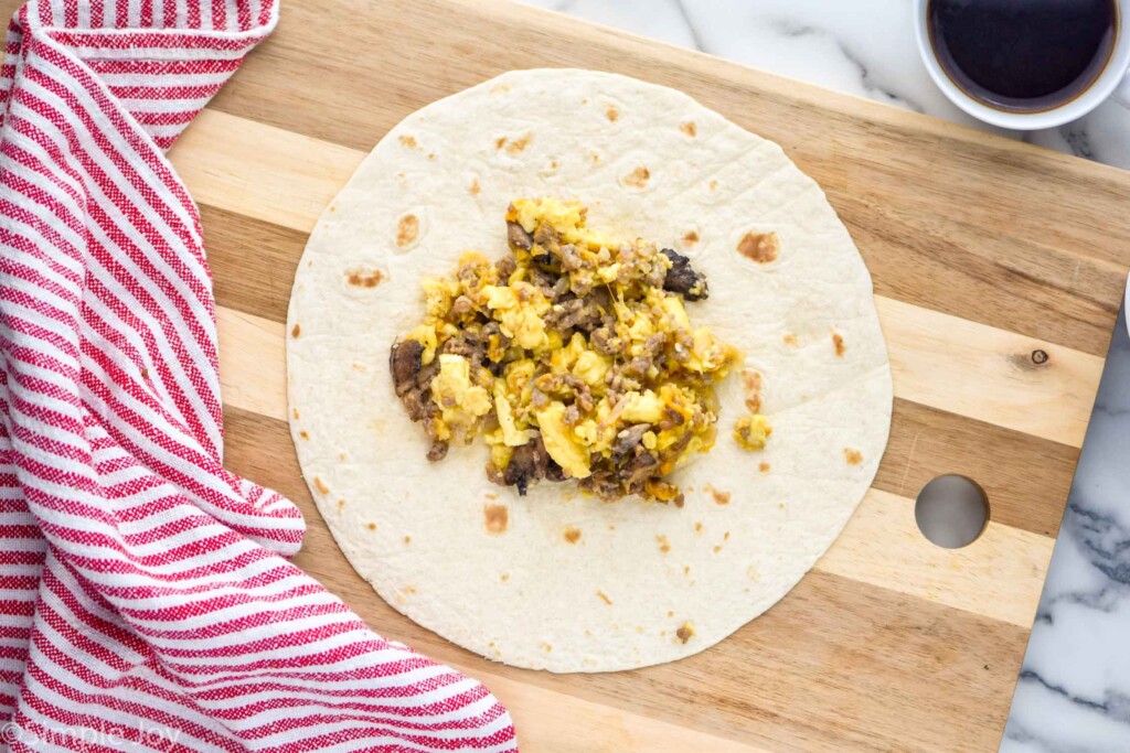 Overhead of flour tortilla on a cutting board with breakfast burrito filling sitting on top