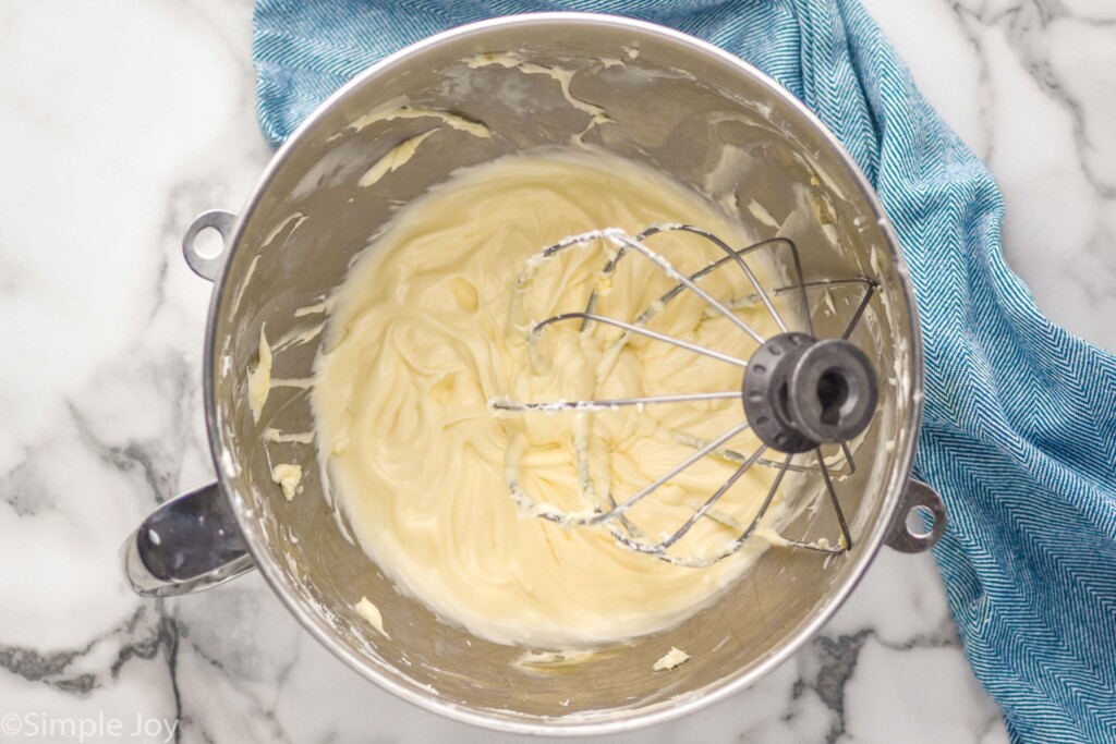 overhead of a mixing bowl with a whisk attachment and cream cheese frosting