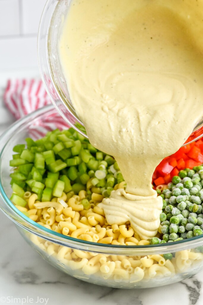 bowl of Macaroni Salad dressing pouring into bowl of Macaroni Salad ingredients