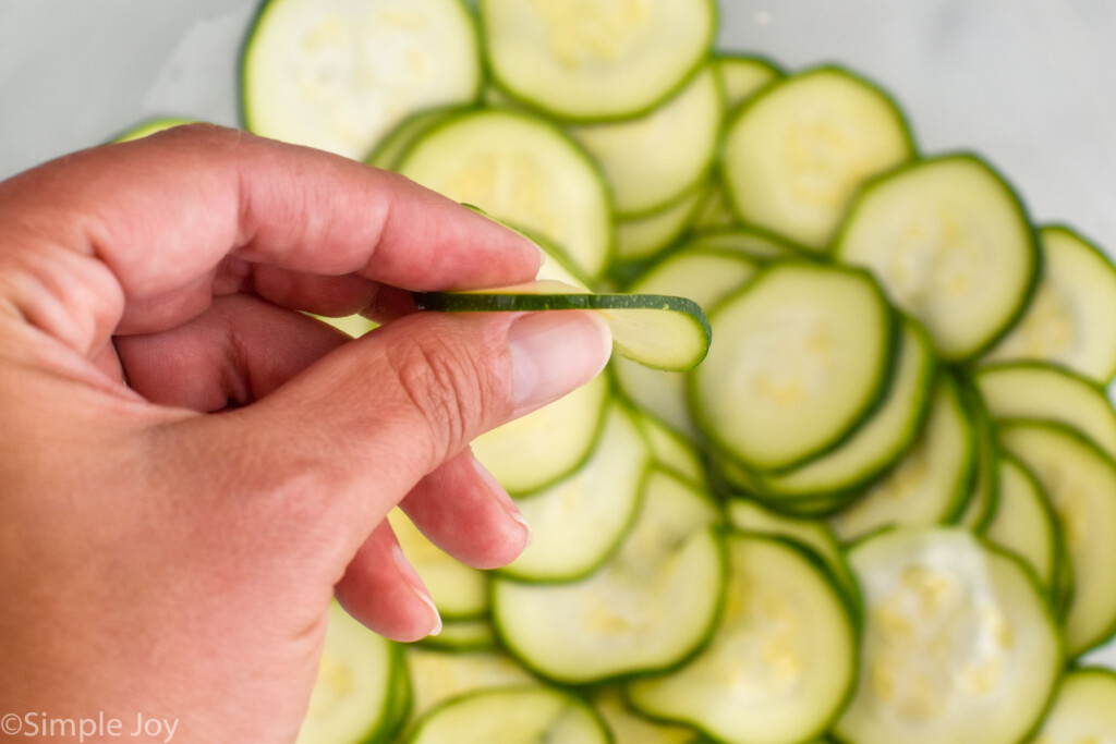 woman's hand holding slice of zucchini over other slices of fresh zucchini to make Italian Zucchini Fritters