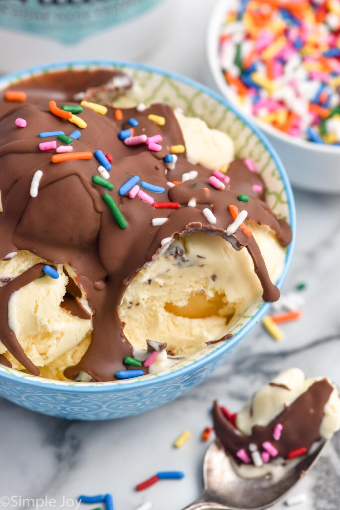 bowl of vanilla ice cream topped with magic shell and sprinkles. Spoon of ice cream and bowl of sprinkles sitting beside