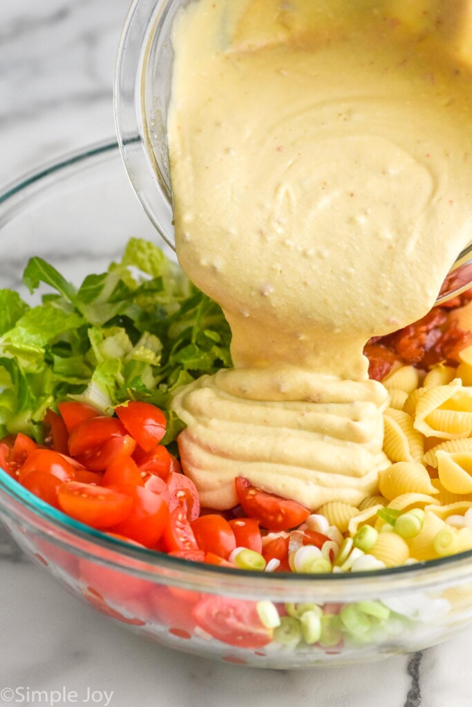 bowl of dressing pouring into a bowl of BLT Pasta Salad ingredients