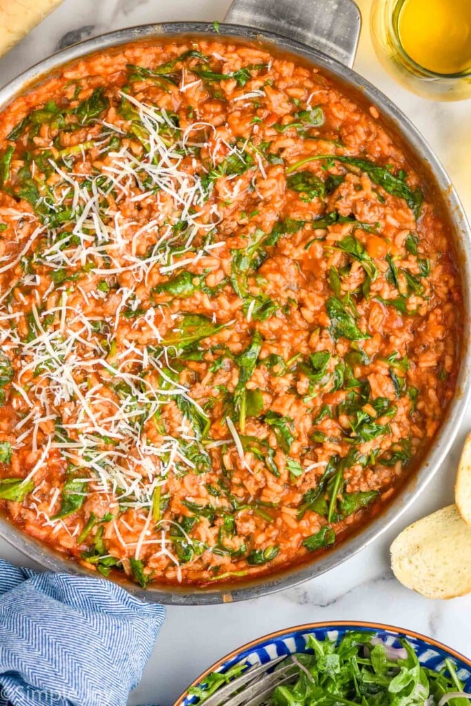 overhead of skillet of risotto with spinach and shredded parmesan cheese